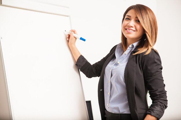 Hermosa joven empresaria hispana escribiendo en un rotafolio y sonriendo durante una presentación de negocios