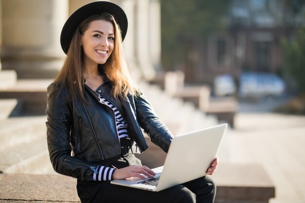 Hermosa joven empresaria trabaja con su computadora portátil de marca en el centro de la ciudad