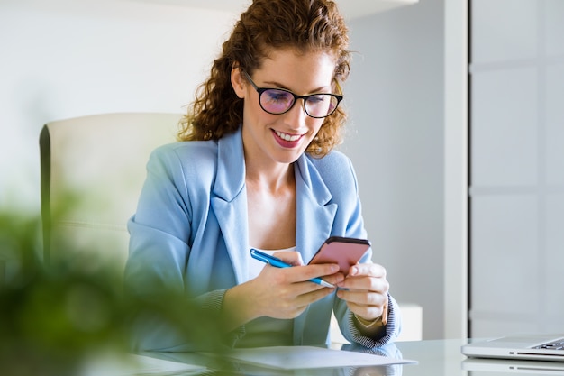 Foto gratuita hermosa joven empresaria usando su teléfono móvil en la oficina.