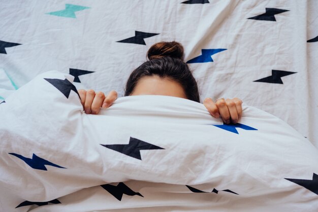 Hermosa joven se encuentra en la cama cubierta con una manta