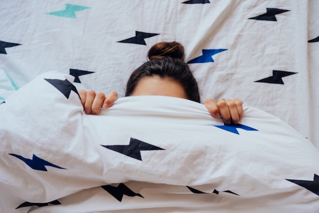 Hermosa joven se encuentra en la cama cubierta con una manta