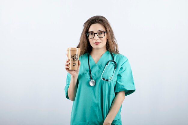Hermosa joven enfermera con estetoscopio sosteniendo una taza de café