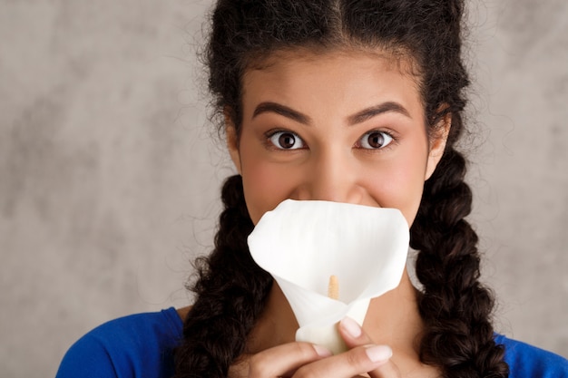 Hermosa joven escondiendo labios detrás de flor blanca