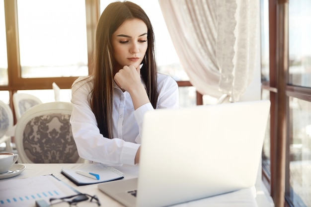 Hermosa joven está analizando información en la computadora portátil