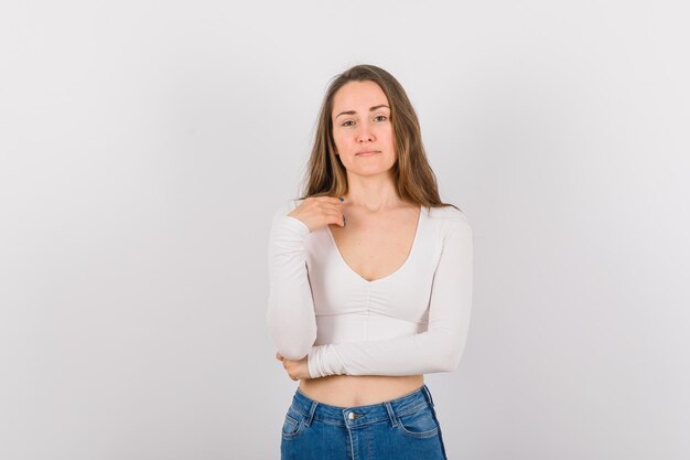 Hermosa joven está mirando a la cámara levantando la mano sobre fondo blanco.