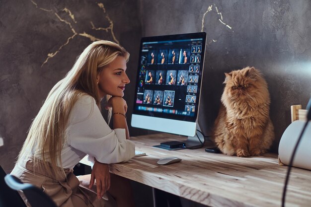 Hermosa joven está sentada al lado de la mesa mientras su gato está sentado en la mesa.