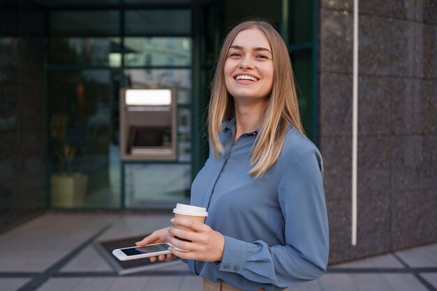 Hermosa joven está usando una aplicación en su dispositivo de teléfono inteligente para enviar un mensaje de texto cerca de edificios comerciales