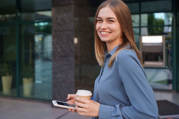 Hermosa joven está usando una aplicación en su dispositivo de teléfono inteligente para enviar un mensaje de texto cerca de edificios comerciales