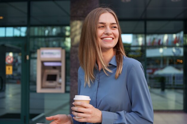 Hermosa joven está usando una aplicación en su dispositivo de teléfono inteligente para enviar un mensaje de texto cerca de edificios comerciales