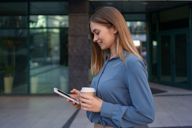 Hermosa joven está usando una aplicación en su dispositivo de teléfono inteligente para enviar un mensaje de texto cerca de edificios comerciales