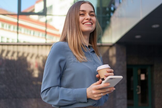 Hermosa joven está usando una aplicación en su dispositivo de teléfono inteligente para enviar un mensaje de texto cerca de edificios comerciales