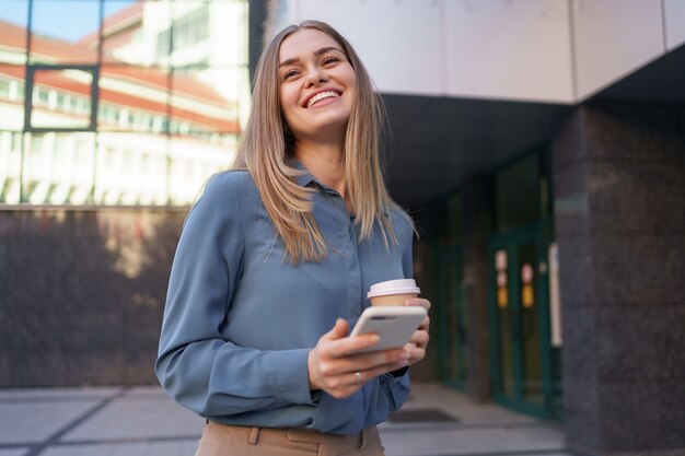 Hermosa joven está usando una aplicación en su dispositivo de teléfono inteligente para enviar un mensaje de texto cerca de edificios comerciales