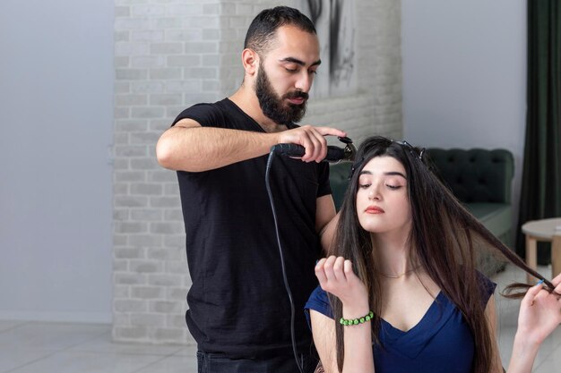 Hermosa joven estirando su cabello mientras peluquero le da forma al cabello Foto de alta calidad