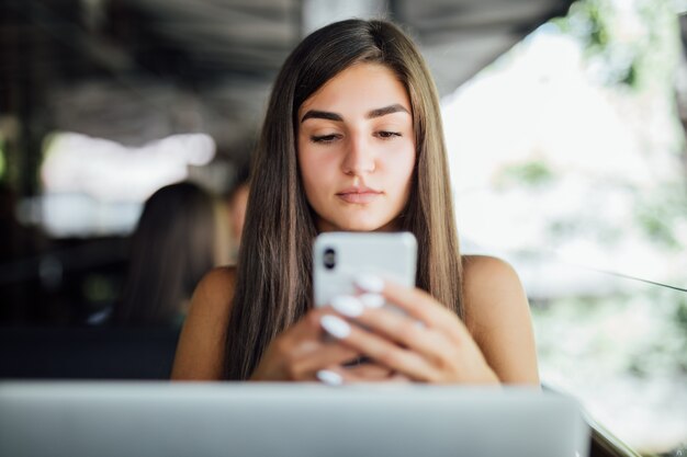 Hermosa joven estudiante con laptop y taza de té o café en la cafetería