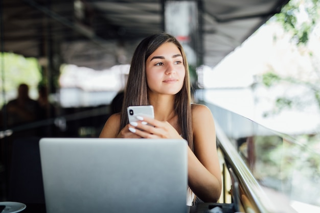 Hermosa joven estudiante con laptop y taza de té o café en la cafetería