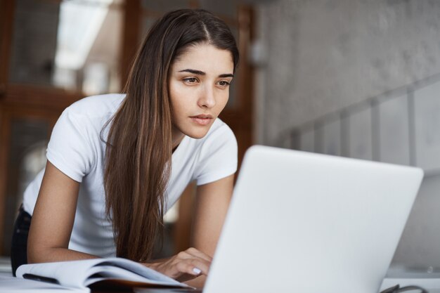 Hermosa joven estudiante navegando por internet en una computadora portátil en busca de nueva información en la biblioteca de la universidad.