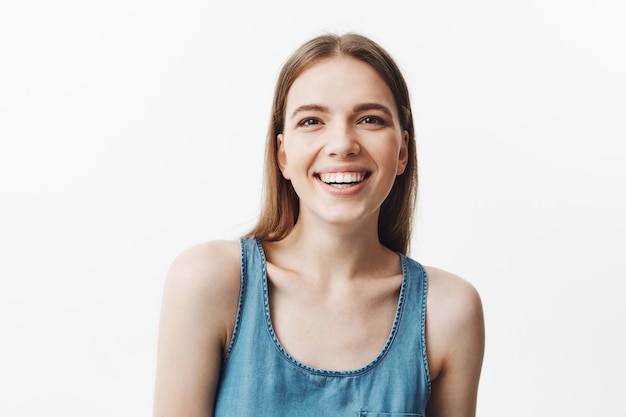 Hermosa joven europea joven con cabello oscuro y elegante peinado en camisa azul riendo a carcajadas en broma divertida, con expresión de la cara feliz y tranquila. Emociones positivas.