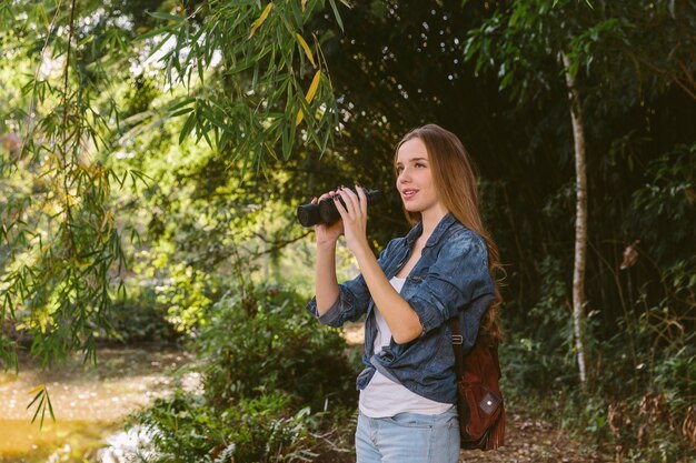 Hermosa joven excursionista mujer sosteniendo binoculares en el bosque