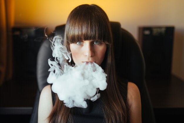 Hermosa joven exhalando humo de una pipa de agua y mirando a la cámara