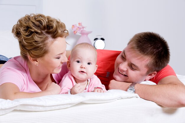 Hermosa joven familia feliz con bebé sonriente acostado en la cama en casa