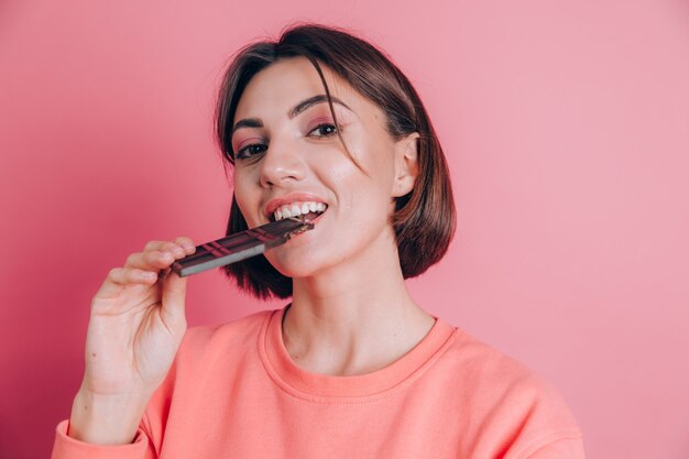 Hermosa joven feliz con barra de chocolate sobre fondo rosa y maquillaje brillante