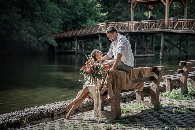 Una hermosa joven con flores y su esposo están sentados en un banco y disfrutan de la comunicación, una cita en la naturaleza, un romance en el matrimonio.