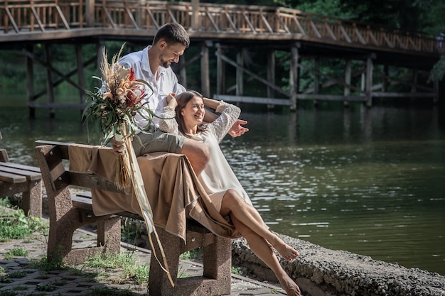 Una hermosa joven con flores y su esposo están sentados en un banco y disfrutan de la comunicación, una cita en la naturaleza, un romance en el matrimonio.