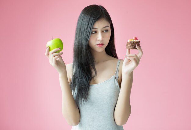 Hermosa joven haciendo una elección entre un pastel y una manzana