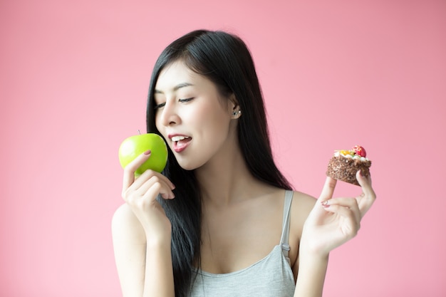 Hermosa joven haciendo una elección entre un pastel y una manzana