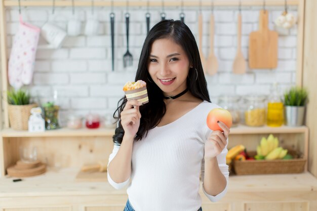 Hermosa joven haciendo una elección entre un pastel y una manzana