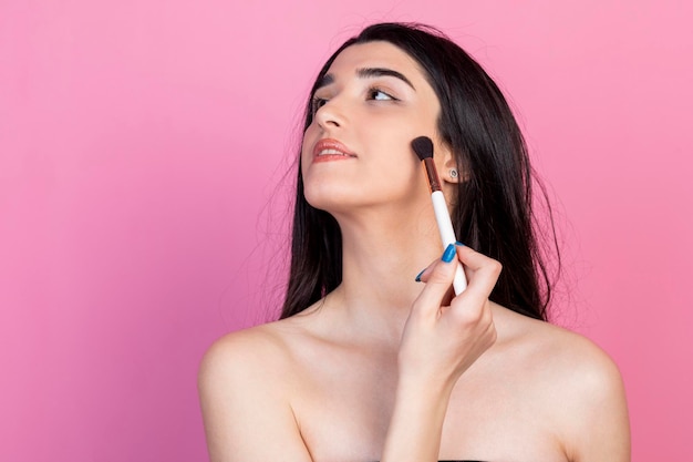 Hermosa joven haciendo maquillaje sobre fondo rosa Foto de alta calidad