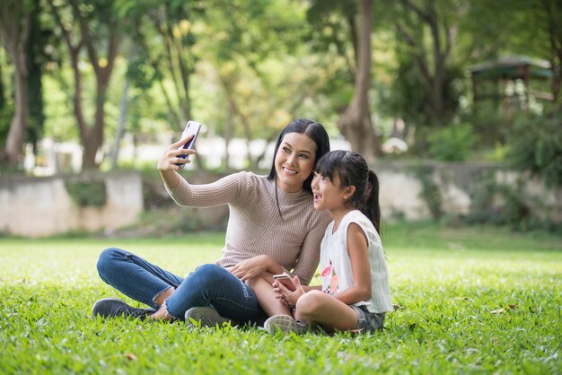 Hermosa joven hija usando teléfono inteligente con su madre al aire libre en el parque