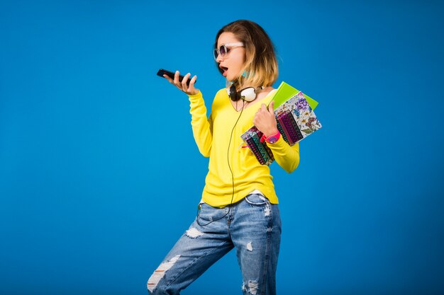 Hermosa joven inconformista sosteniendo libros y mirando smartphone