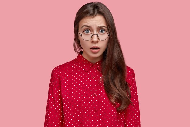 Hermosa joven indignada siente resentimiento y malentendido, usa gafas redondas y camisa elegante