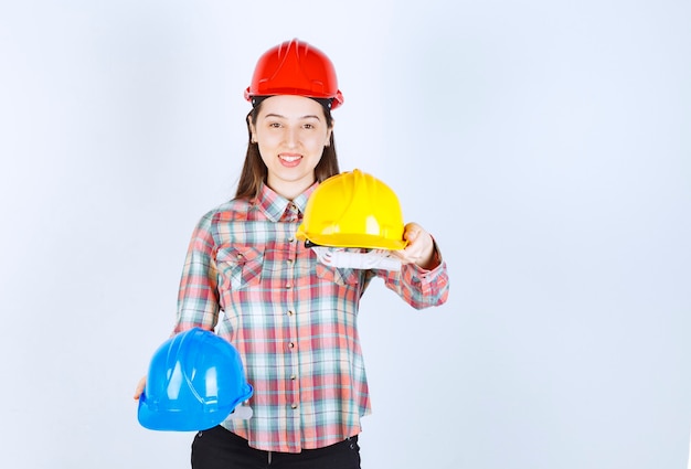 Hermosa joven ingeniero con cascos de seguridad y de pie sobre fondo blanco.