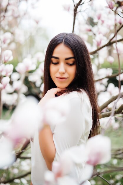 Hermosa joven en un jardín floreciente con magnolias. Floración de magnolia, ternura.