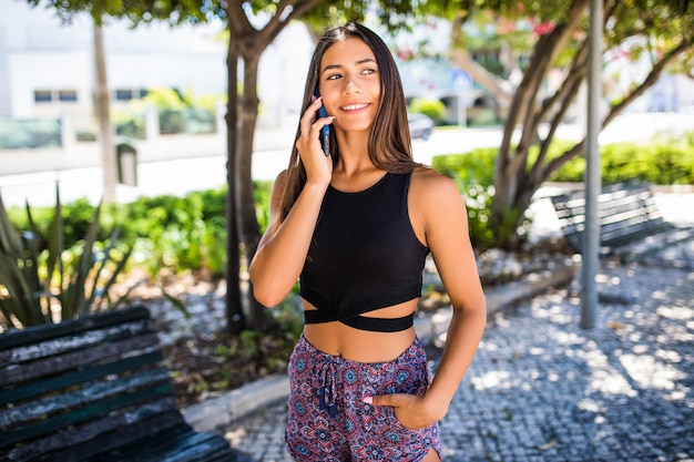 Hermosa joven latina hablando por teléfono mientras camina por la calle