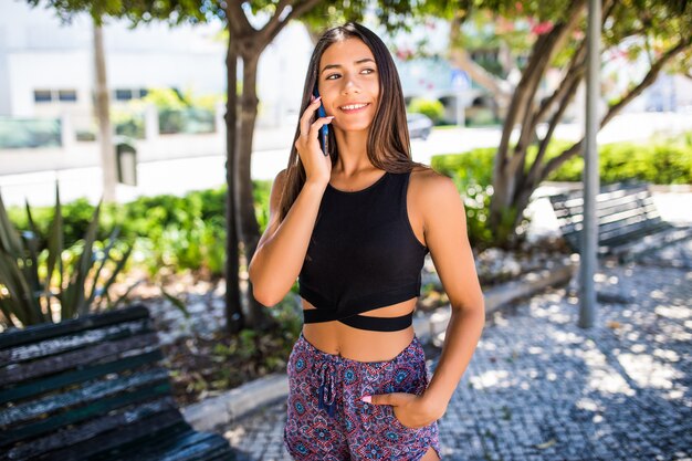 Hermosa joven latina hablando por teléfono mientras camina por la calle