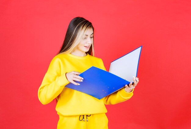 Hermosa joven leyendo documentos dentro de la carpeta azul en la pared roja