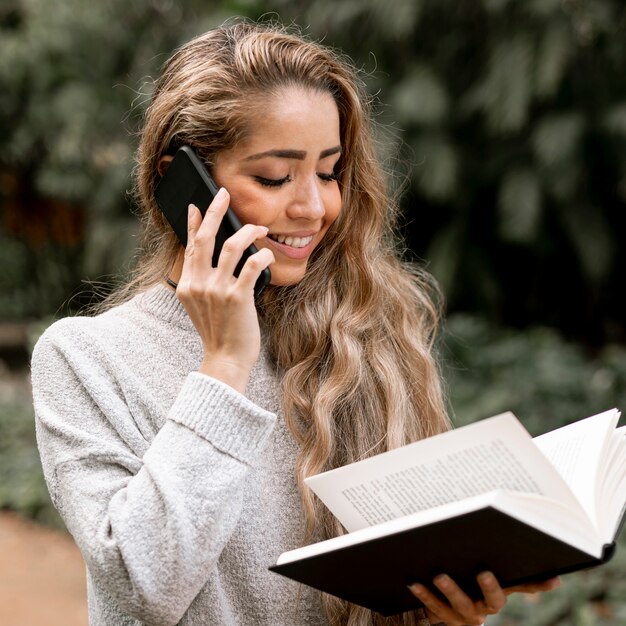 Hermosa joven leyendo un libro mientras habla por teléfono