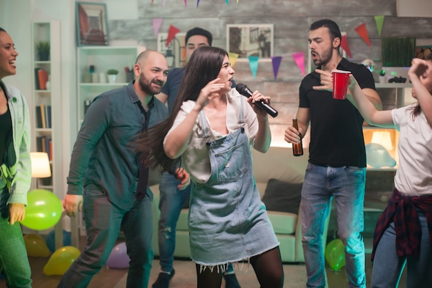 Hermosa joven llena de felicidad haciendo karaoke para sus amigos en la fiesta.