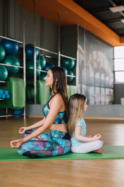 Hermosa joven madre y su hija están meditando mientras están sentados en pose de yoga