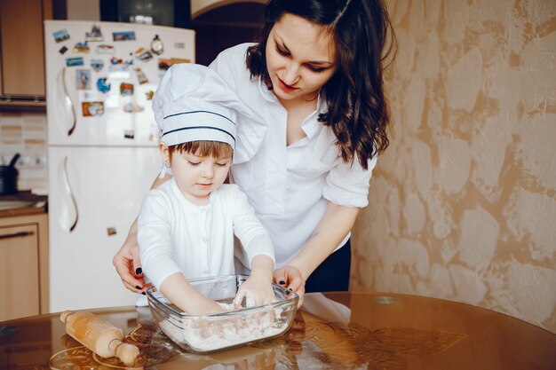 Una hermosa joven madre con su pequeña hija está cocinando en la cocina en casa