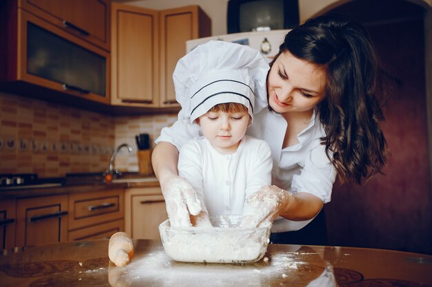 Una hermosa joven madre con su pequeña hija está cocinando en la cocina en casa