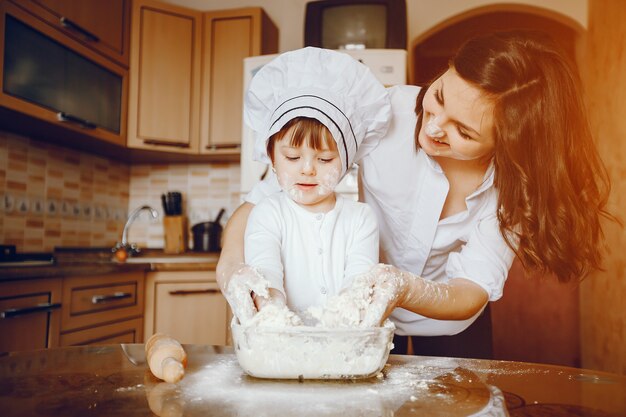 Una hermosa joven madre con su pequeña hija está cocinando en la cocina en casa