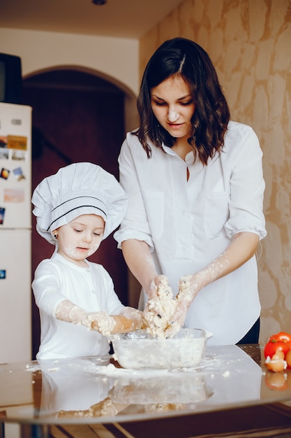 Una hermosa joven madre con su pequeña hija está cocinando en la cocina en casa