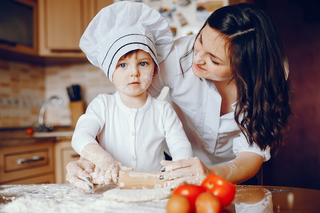 Una hermosa joven madre con su pequeña hija está cocinando en la cocina en casa