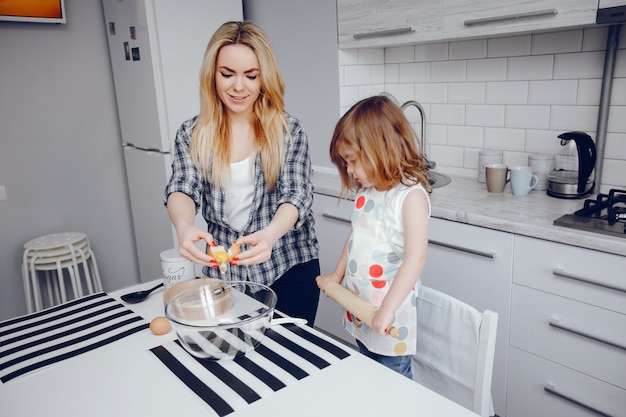 Una hermosa joven madre con su pequeña hija está cocinando en la cocina en casa