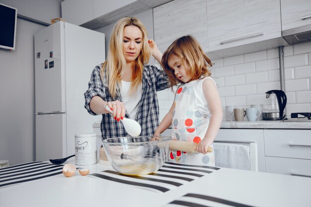 Una hermosa joven madre con su pequeña hija está cocinando en la cocina en casa