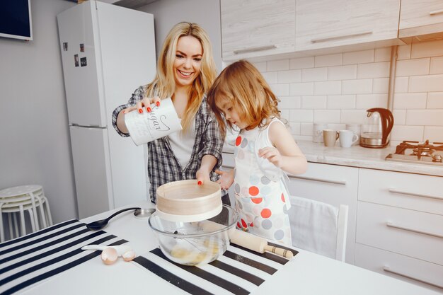 Una hermosa joven madre con su pequeña hija está cocinando en la cocina en casa